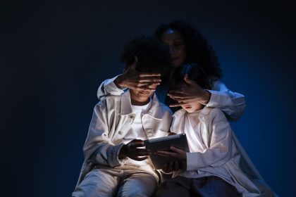 Mãe supervisiona duas crianças enquanto elas usam um tablet em casa.