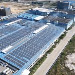 Vista aérea de painéis solares instalados sobre um complexo industrial.
