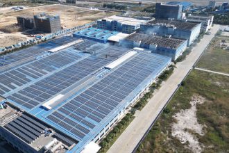 Vista aérea de painéis solares instalados sobre um complexo industrial.