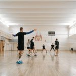 Crianças participam de um treino de voleibol em uma quadra coberta.
