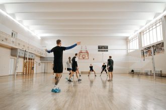 Crianças participam de um treino de voleibol em uma quadra coberta.