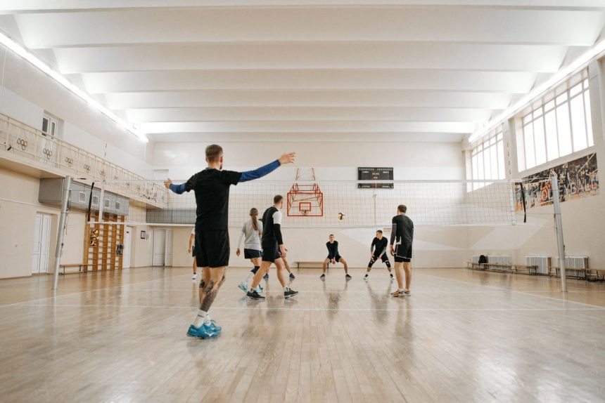 Crianças participam de um treino de voleibol em uma quadra coberta.