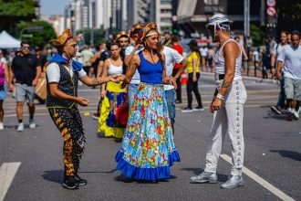 Artistas em trajes tradicionais realizam apresentação de dança em uma rua durante evento cultural no Brasil.
