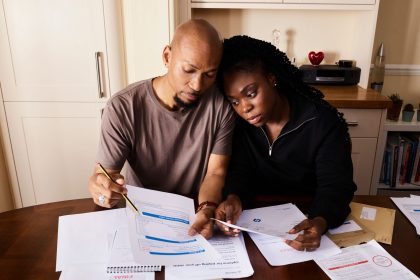 Casal sentado à mesa revisa documentos financeiros e organiza o orçamento doméstico.